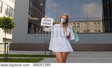 Girl In Protective Mask With Shopping Bags Showing Black Friday Inscription, Looking Satisfied With 