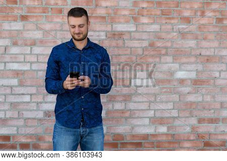 Handsome British Man Sending Message To Girlfriend With Mobile Phone In Front Of Brickstone Wall In 