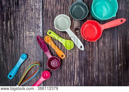 Colorful Measuring Cups And Measuring Spoons Use In Cooking Lay On Dark Brown Wood Tabletop.