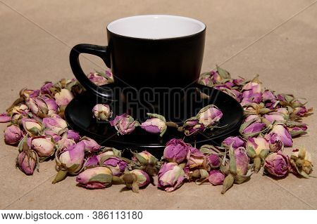 A Black Mug With A Saucer With Tea Made From Dried Buds And Petals Of A Purple Damask Rose Stands On