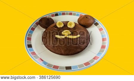 Brown Cacke In Shape Of Bear Head On Plate. Isolated On Yellow Background. Cupcake With Eyes, Nose A