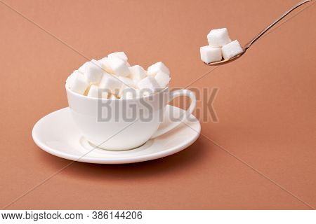 White Cup Of Coffee Is Overfilled With Sugar Cubes. Too Sweet Beverage Concept. Isolated On Brown Su