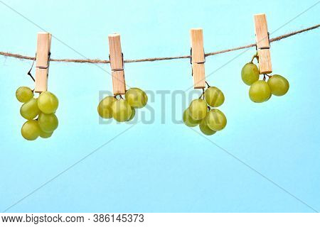 Bunches Of Grape Are Hanging On Clothpins. Clothline String With Fruits Isolated On Blue Background.