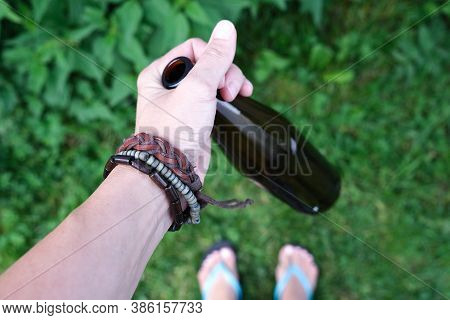 A Hand Of A Hippie, Hipster Holding A Bottle Of Alcohol, Beer. Young People With Alcohol Addiction C
