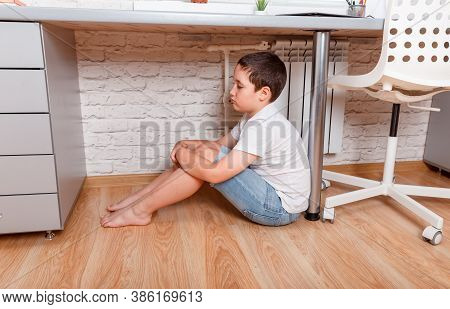 Unhappy Kid Boy Sitting Under Desk. Teen Feeling Anxious. Child Suffering From Loneliness. Junior Hi