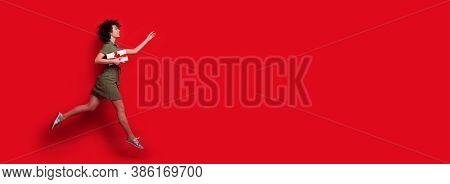 Caucasian Woman With Curly Hair Running After Something To Give A Box With Present Posing On A Red S