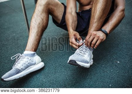 Young Man Exercising Outside. Cut View Of Sportsman Sitting On Fround And Tie Shoe Laces. Preparing 