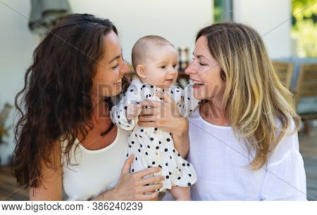 Woman With Daughter And Baby Granddaughter Resting Outdoors In Backyard.