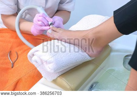 Pedicurist Woman Removes Cuticle From Clients Toes Using Electric Nail Machine, Closeup View. Profes