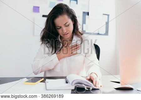 Beautiful Woman Sick With Feeling Pain In The Chest While Working With Papers. Hand Holding Chest Af