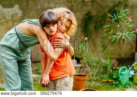 Blond Female Gardener Hugging Her Cute Child Son With Down Syndrome, Caressing And Colm Down