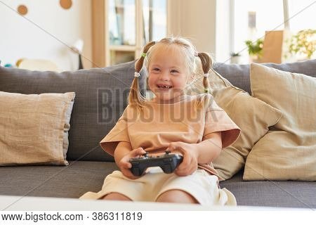 Portrait Of Cute Girl With Down Syndrome Playing Video Games And Laughing Happily While Sitting On C