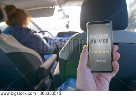 Passenger is sitting on the back seat of the car and using smart phone app to rate a driver. Taxi or modern peer to peer ridesharing concept