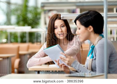 Two girls communicate sitting at the table at the reading hall. Process of communication