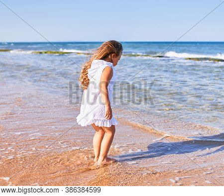 Adorable blonde child on back view wearing summer dress playing on the sand at the beach