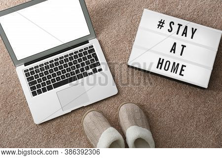Laptop, Slippers And Lightbox With Hashtag Stay At Home On Soft Carpet, Flat Lay. Message To Promote