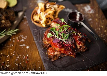 Pork ribs cooked at low temperature. Blackcurrant sauce, parsnip chips with Parmesan cheese. Delicious healthy meat food closeup served on a table for lunch in modern cuisine gourmet restaurant.