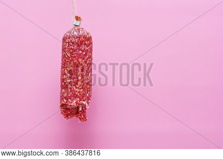 A Piece Of Semi-smoked Sausage Hangs On A Pink Background. Close Up.
