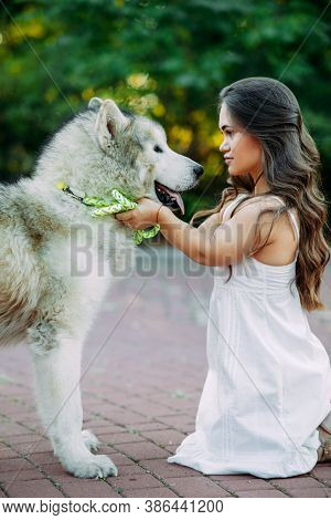 Young Woman With Innate Disorder Dwarfism Embraces Malamute Dog While Walking In Park.