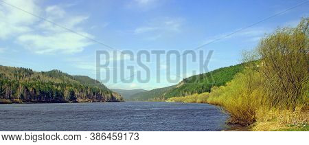 A Wide River Runs Slowly Towards The Wooded Mountains.