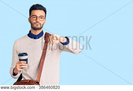 Young handsome hispanic man wearing leather bag and drinking take away coffee with angry face, negative sign showing dislike with thumbs down, rejection concept 