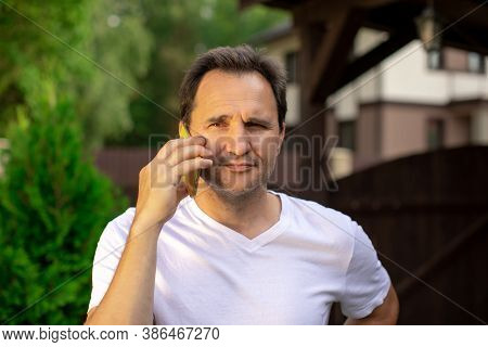 Closeup Portrait View Of One Handsome Unshaven Pensive 40s Man In White T-shirt Speaking On Mobile P