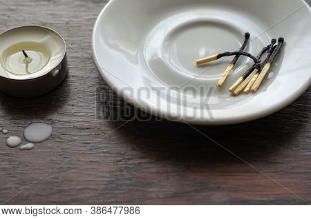 A Darkened Small Candle On A Wooden Table. Next To The Wax Camles On The Table And Burnt Matches In 