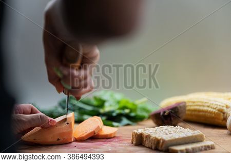 Low Angle View Of A Woman Cutting Sweet Potato On A Cutting Board Full Of Vegetables And Tempeh Prot