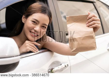 Asian Young adult in car holding disposable bag for take out food from drive thru service restaurant. Drive thru is new normal and popular service after coronavirus covid-19 pandemic.