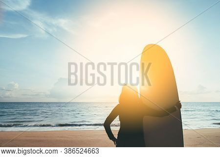 Woman Hold Surfboard Standing At Tropical Sunset Beach Background. Summer Vacation And Sport Adventr