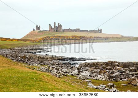 Dunstanburgh castle s polem trávu zelenou louku v Northumberlandu Anglie UK