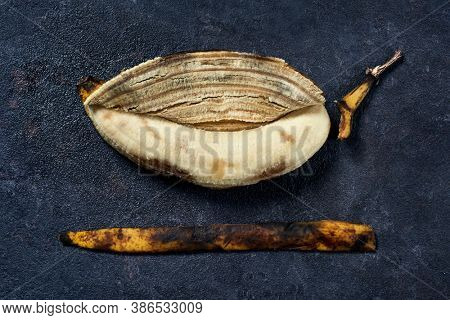 high angle view of a peeled overripe banana and its skin on a black stone surface