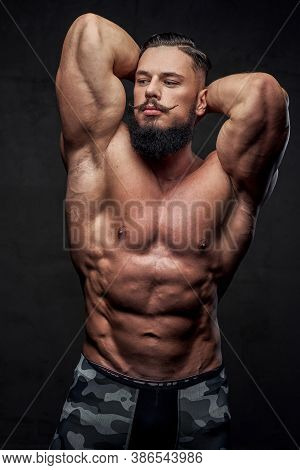 Brutal Military Athlete With Naked Torso And With Beard And Mustache Posing In Dark Gray Background.