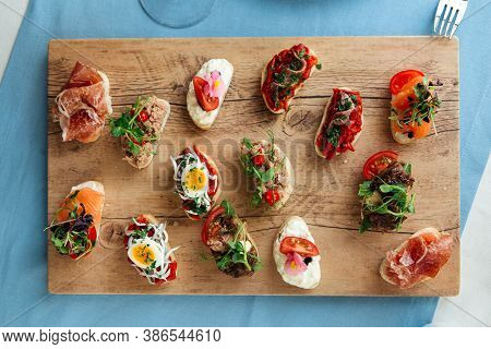Top View On Assorted Variety Of Tappas With Different Toppings On The Wooden Board