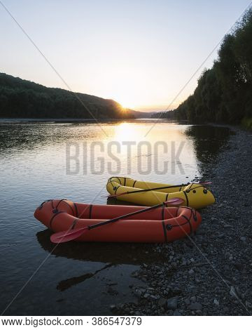 Orange and yellow packrafts rubber boats with padles on a sunrise river. Packrafting. Active lifestile concept
