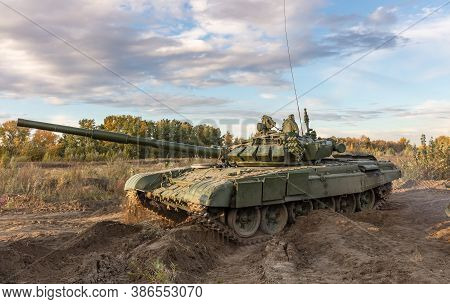 A Side Shot Of Russian Tank Turning T-64 In The Field. Blue Cloudy Sky As A Background.