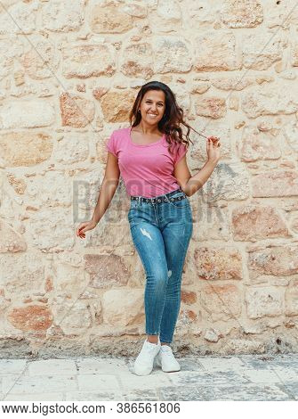 Young Women Wearing T-shirt And Jeans Stays Near A Wall And Smile