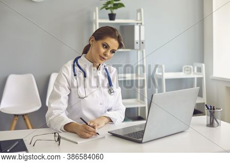 Woman Doctor Making Notes During Online Lesson Or Video Call Consultation In Medical Clinic