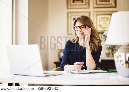 Confident Businesswoman Sitting At Office Desk And Making A Phone Call While Working From Home. Home