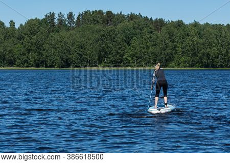A Young Sporty Blonde Woman In The Wetsuit Is Surfing On The Sup Board In The Aquatory Of The Forest