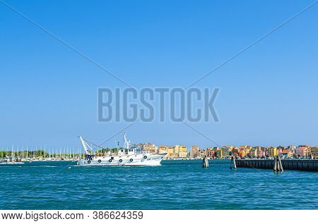 Chioggia, Italy, September 16, 2019: Fishing Ship Boat In Water Of Lagoon With Row Of Colorful Build