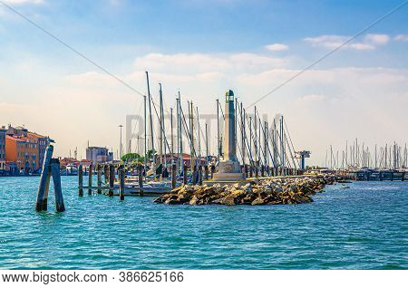 Lighthouse On Stone Pier Of Yacht Port Marina, Wooden Bricole Poles In Water Of Lagoon Near Chioggia