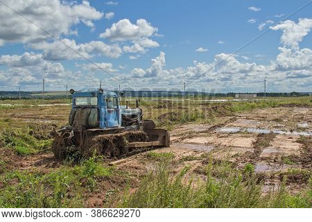 An Old Tracked Tractor In The Background Of The Landscape. Agricultural Machinery In The Field