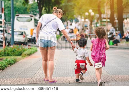 Back View Of Mother Walking On The Pavement With Her Young Son  In The Aftrenoon On Sunny Summer Day