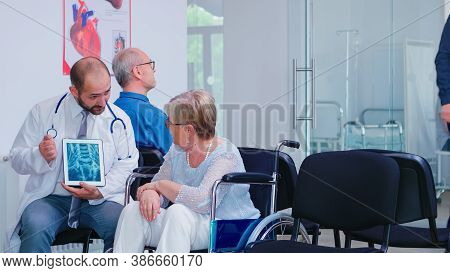 Physician Holding Tablet Pc While Discussing With Disabled Senior Woman In Wheelchair. Man Arriving 