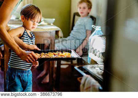 Cute Little Preschooler Boy In Striped T-shirt Help His Mother At Kitchen. Cook At Home. Young Woman