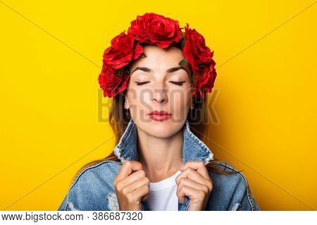 Young Woman With Closed Eyes In A Denim Jacket And A Wreath Of Red Flowers On Her Head On A Yellow B