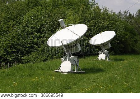 Pair Of White Radio Telescope Antennas On The Dandelion And Grass Field