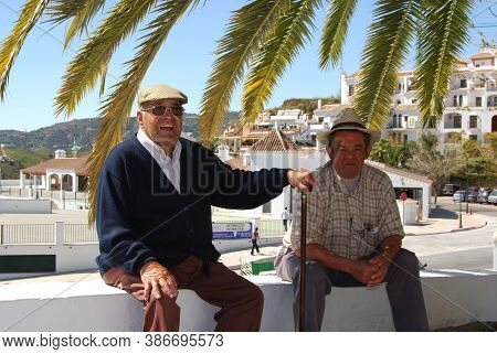 Frigiliana, Spain - March 19, 2008 - Two Old Men Sitting On Wall Under A Palm Tree, Frigiliana, Spai