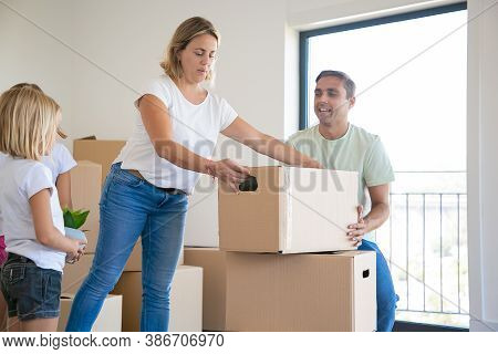 Beautiful Blonde Mother Putting Carton Box On Another One. Happy Family With Two Daughters Moving To
